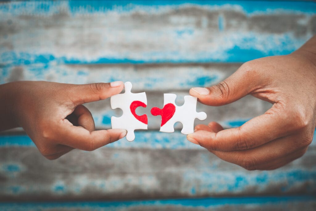 People holding jigsaw puzzle pieces forming a heart shape on a table — supporting a loved one in a halfway house