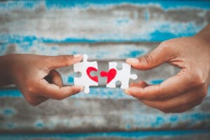 People holding jigsaw puzzle pieces forming a heart shape on a table — supporting a loved one in a halfway house